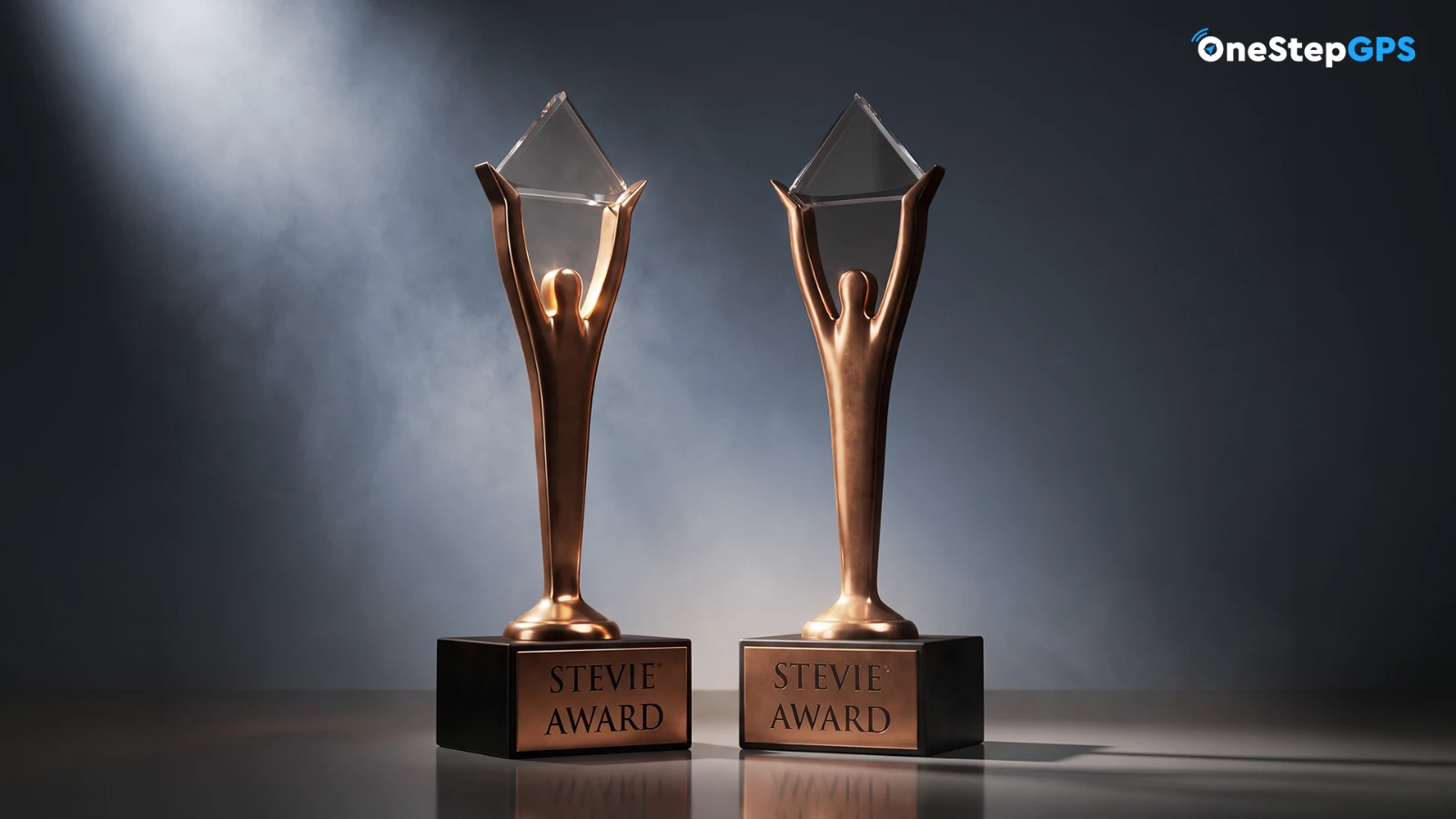 Two bronze Stevie Award trophies lit from behind on a dark background with the One Step GPS logo