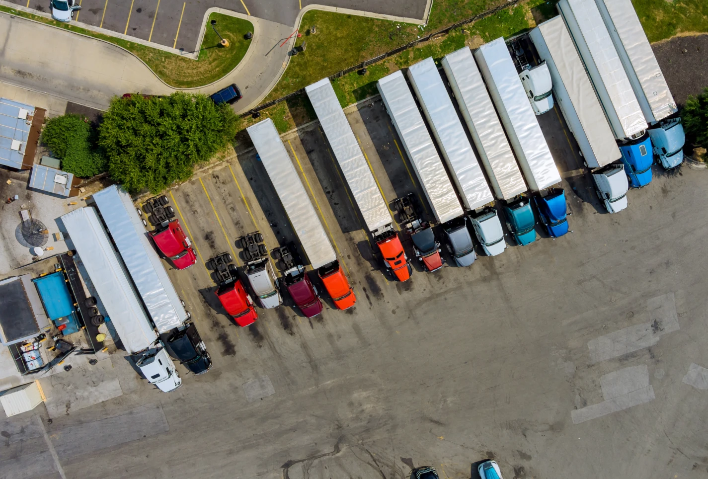 An aerial top-down photo of a row of parked semi-trucks and trailers in a yard, illustrating a large fleet whose data is shared across dispatchers, managers, executives, and IT through role-based access.